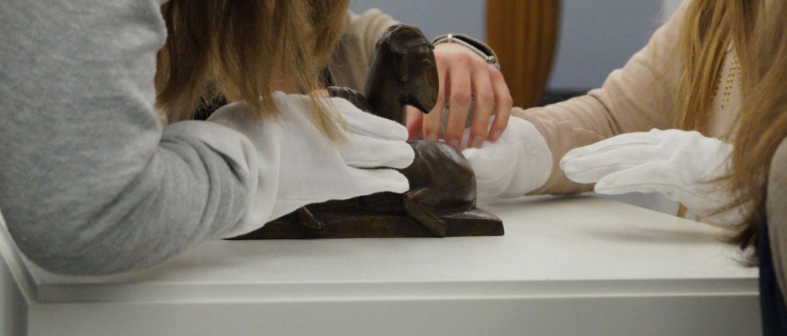 H&auml;nde mit wei&szlig;en Handschuhen ertasten eine Figur in Schafsform.