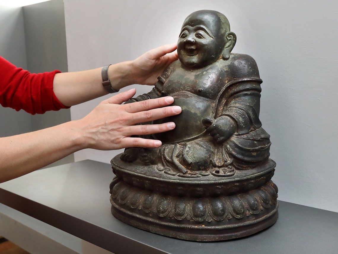 Zwei H&auml;nde ber&uuml;hren eine Buddha-Figur.