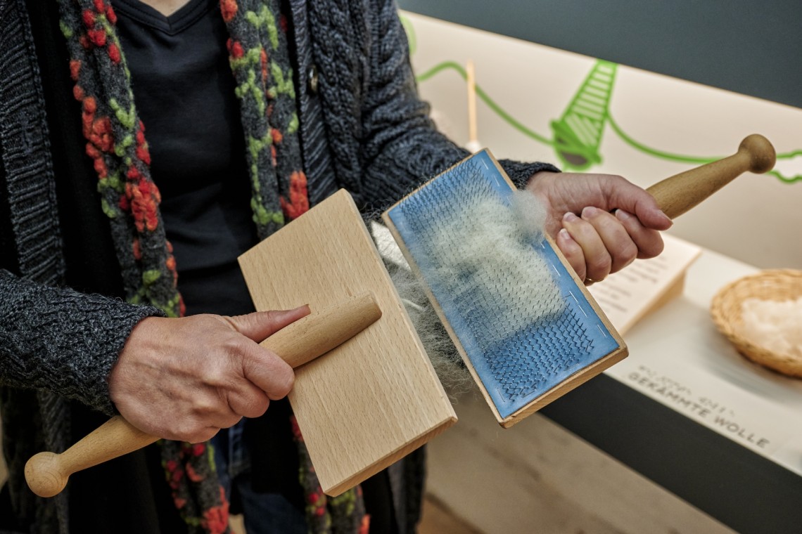 Zwei H&auml;nde halten einen Kamm zur Wollbearbeitung.