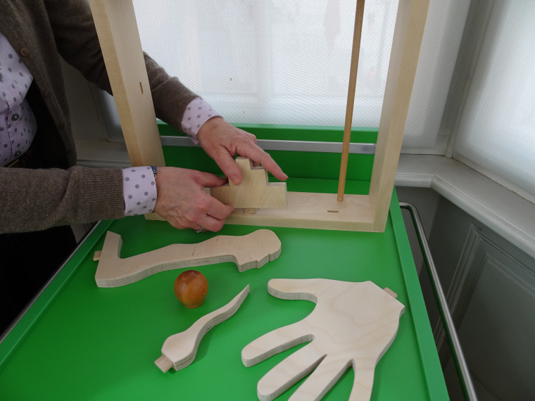 Zwei H&auml;nde setzen verschiedene Holzteile zusammen. Ein Holzteil sieht aus wie eine Handfl&auml;che.