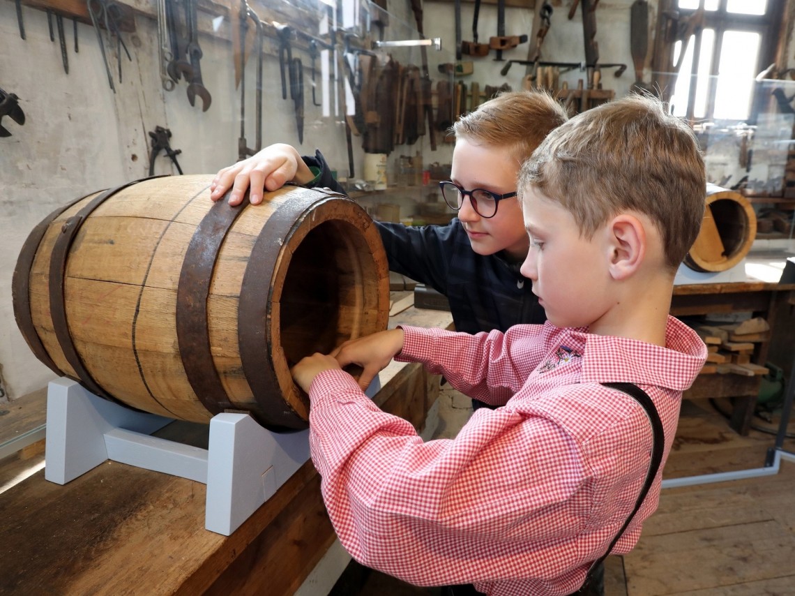 zwei Kinder betasten ein kleines Holzfass.