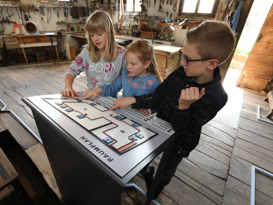 Drei Kinder ber&uuml;hren einen tastbaren Lageplan in einer historischer Werkstatt.