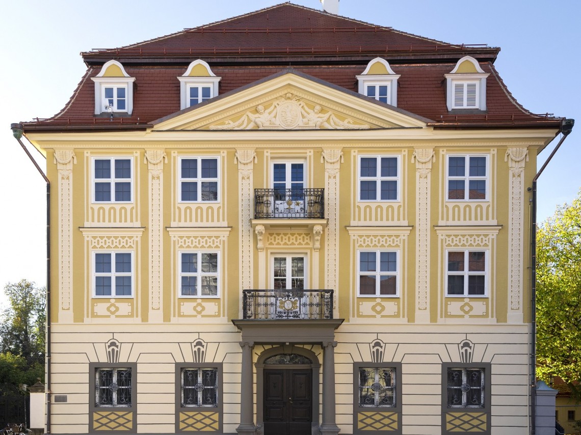 Ein dreigeschossiges Geb&auml;ude mit gro&szlig;em Eingangsportal und Walmdach. Es sieht majest&auml;tisch aus.