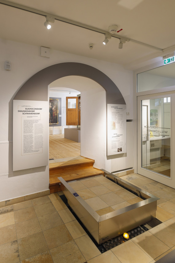 Ein Hublift ist vor zwei Treppenstufen in einem Ausstellungsraum installiert.