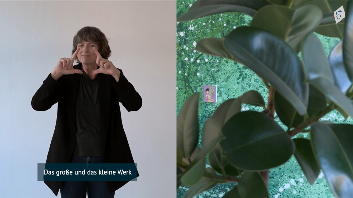 Auf dem zweigeteilten Filmausschnitt zur Ausstellung "We Are Plants" ist links die Museum Signerin Birgit Fehn frontal zu sehen. Sie geb&auml;rdet gerade "Das gro&szlig;e und das kleine Werk". Passend dazu ist rechts hinter den gro&szlig;en Bl&auml;ttern einer Zimmerpflanze eine Wand f&uuml;llende pflanzenartig wirkende &Ouml;lmalerei des K&uuml;nstlers Reiner Heidorn mit einem darauf angebrachten kleinen Portr&auml;tbild von Katrin Bittl zu sehen
