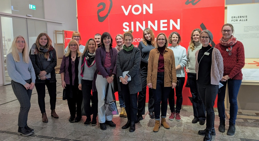 Eine Gruppe von Menschen steht vor einer roten Wand mit der Aufschrift "Von Sinnen" und sieht in die Kamera.